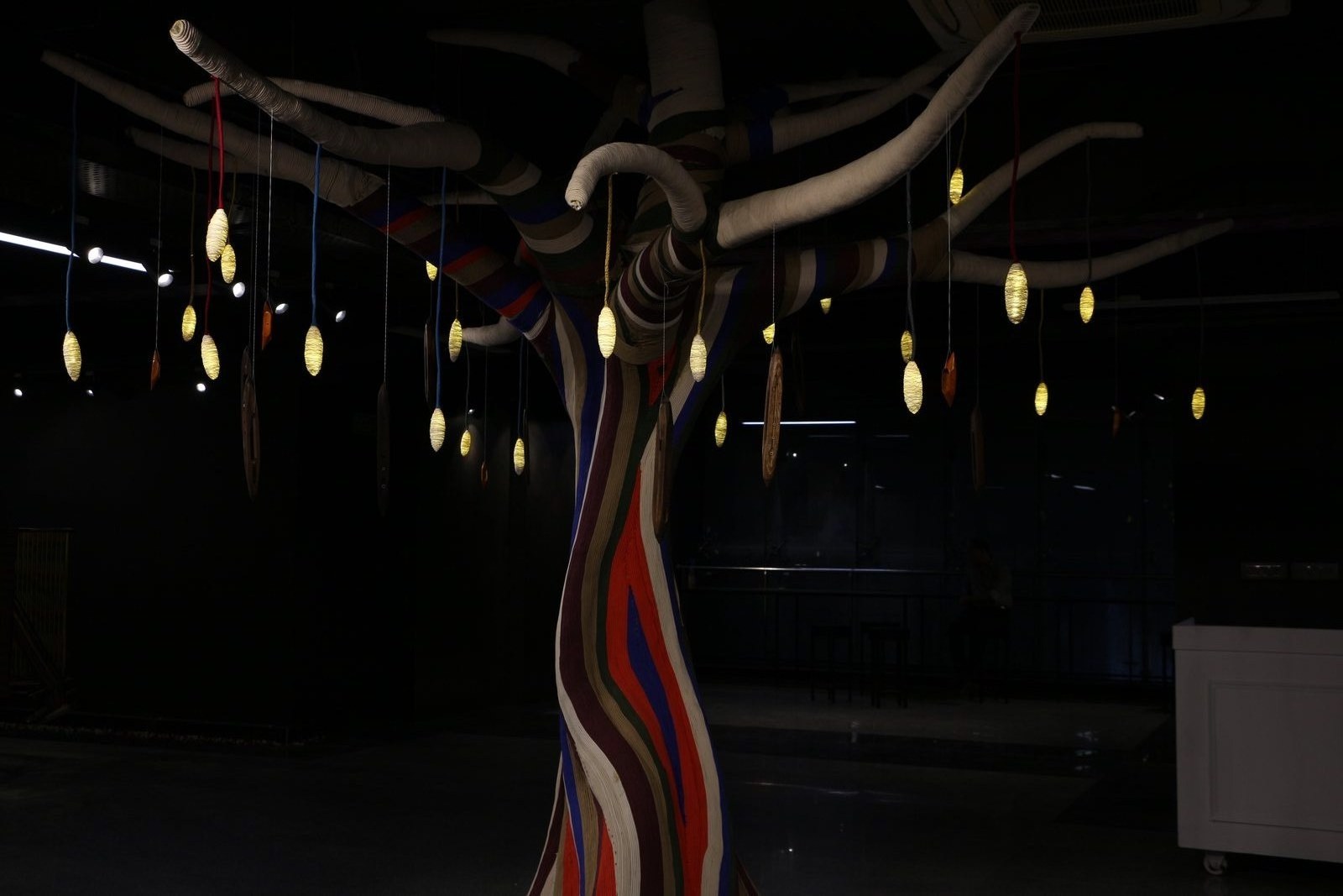 Multicolored twisted textile strands installation suspended with hanging pendant lights.