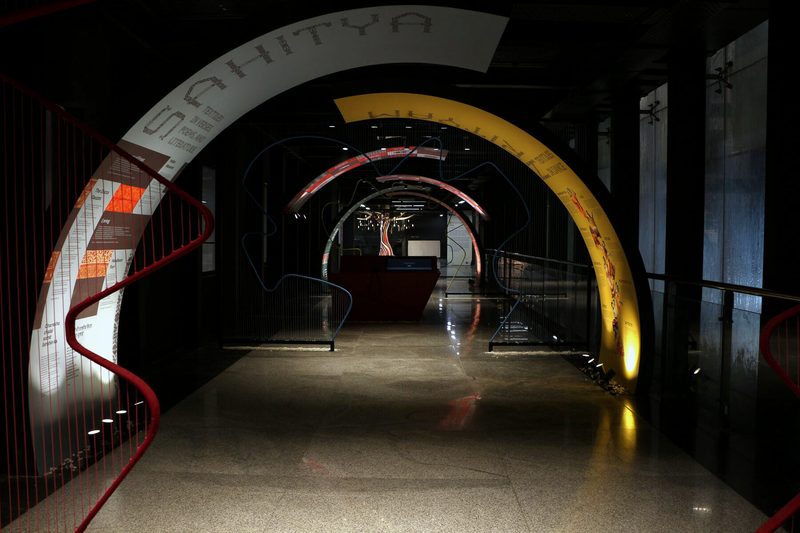 Illuminated tunnel passageway with concentric arches in red and gold architectural colors.